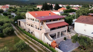 Um edifício residencial de vários andares com telhado vermelho, uma área externa coberta com assentos e vista para casas e vegetação ao redor.
