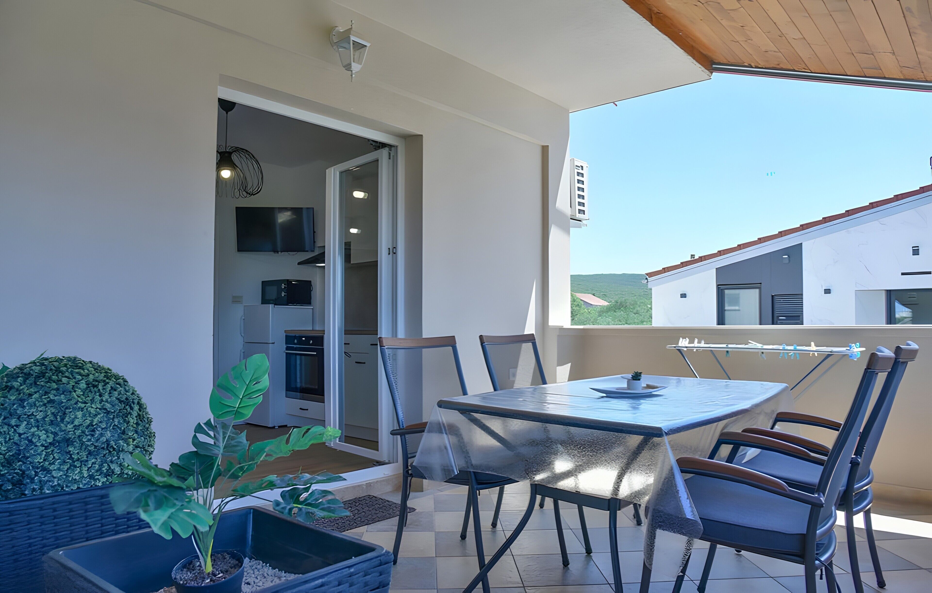 A covered outdoor dining area with a table and chairs, a potted plant, and a view of a house in the background.