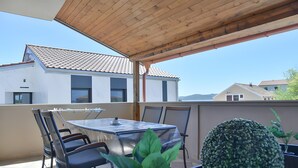Um pátio externo com mesa e cadeiras, um vaso de planta e vista para um edifício com telhado em azulejos.