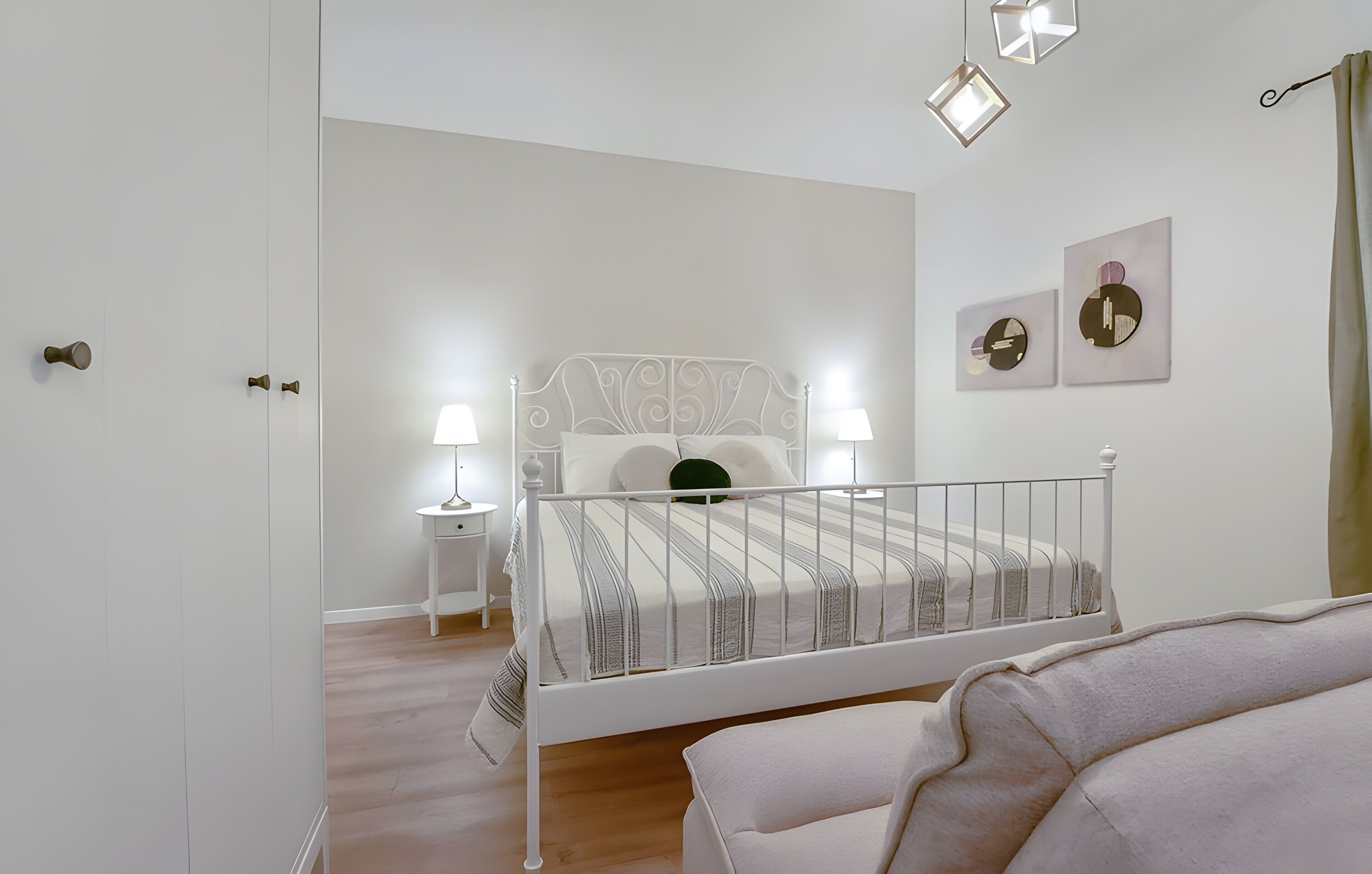 A bedroom with a white metal bed frame, a bedside table with a lamp, and a wall with abstract art.