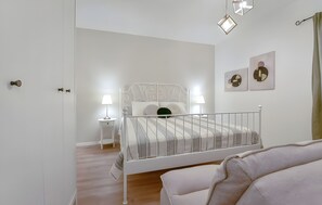 Een slaapkamer met een bed met wit metalen frame, een nachtkastje met een lamp en een muur met abstracte kunst.