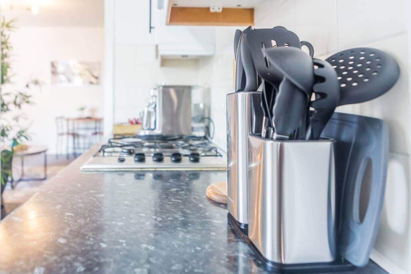 Une cuisine équipée d’une hotte en acier inoxydable, d’une cuisinière à gaz et d’un porte-ustensiles sur le plan de travail.