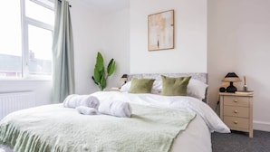 A hotel room with a bed, a nightstand, a lamp, and a window with curtains. - The Geordie Getaway! (Newcastle upon Tyne)
