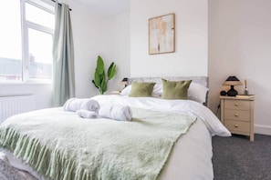 A hotel room with a bed, a nightstand, a lamp, and a window with curtains. - The Geordie Getaway! (Newcastle upon Tyne)