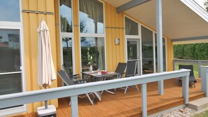 En moderne terrasse med spiseplads, store vinduer og gelænder af træ.