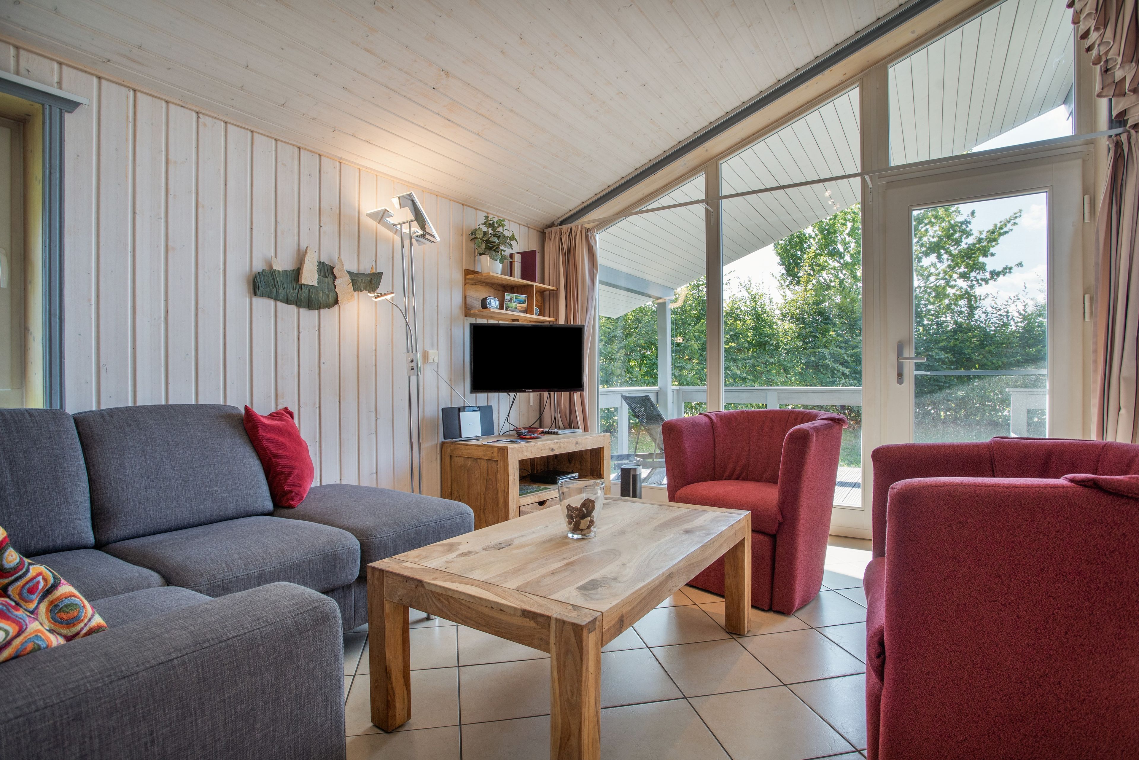 Un salon moderne avec un canapé gris, un fauteuil rouge, une table basse en bois et un téléviseur à écran plat.