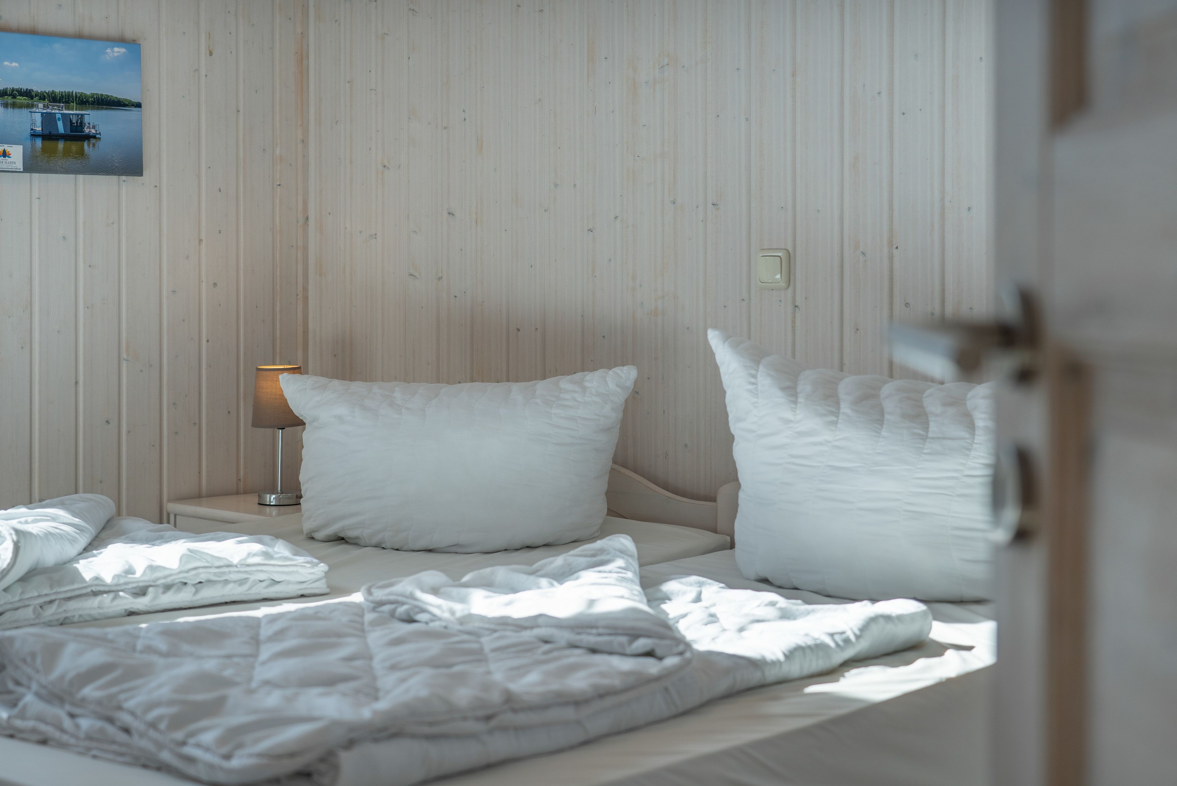 A hotel room with a bed, pillows, a bedside lamp, and a framed picture on the wall.