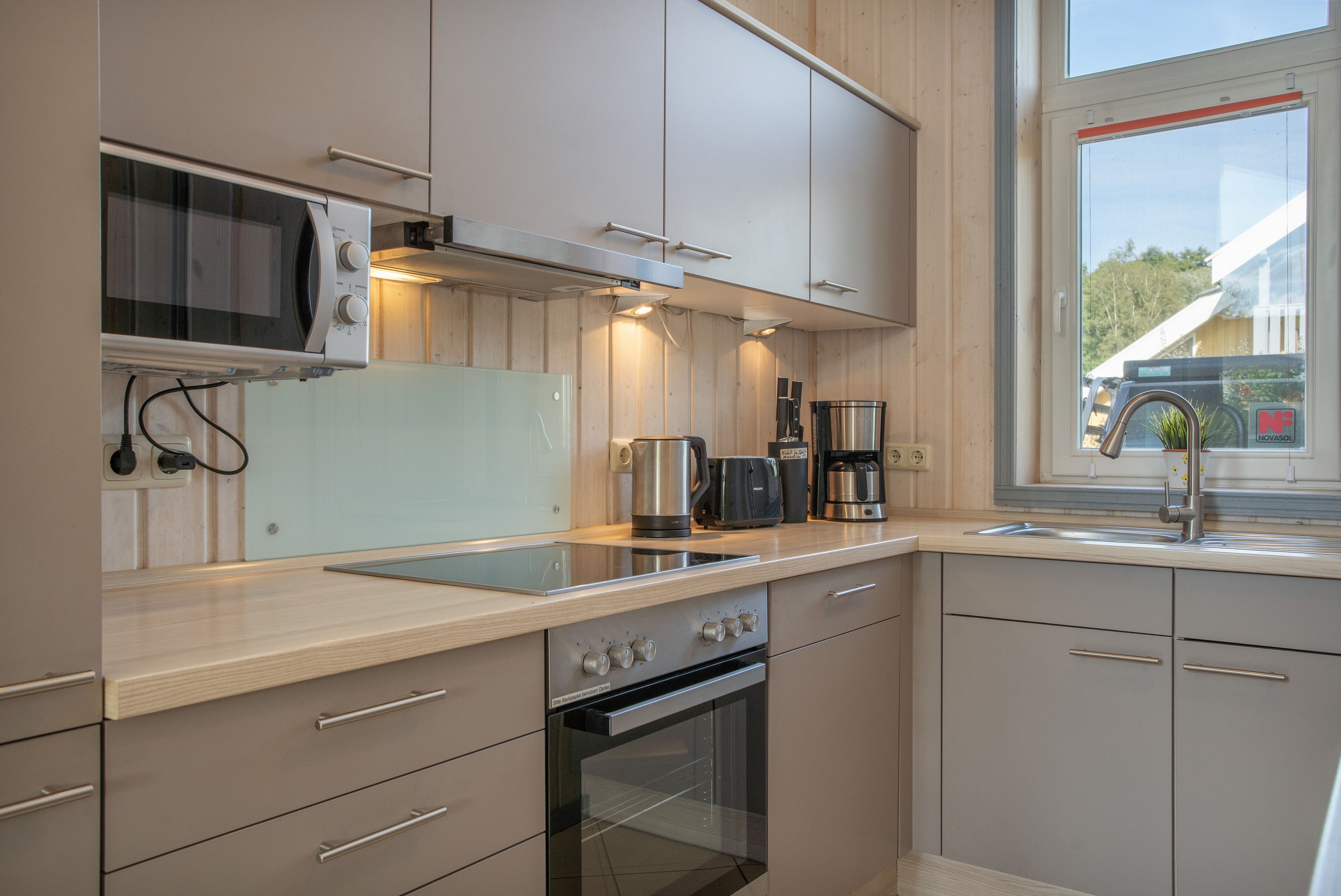 A modern kitchen with stainless steel appliances, wooden cabinetry, and a window providing natural light.