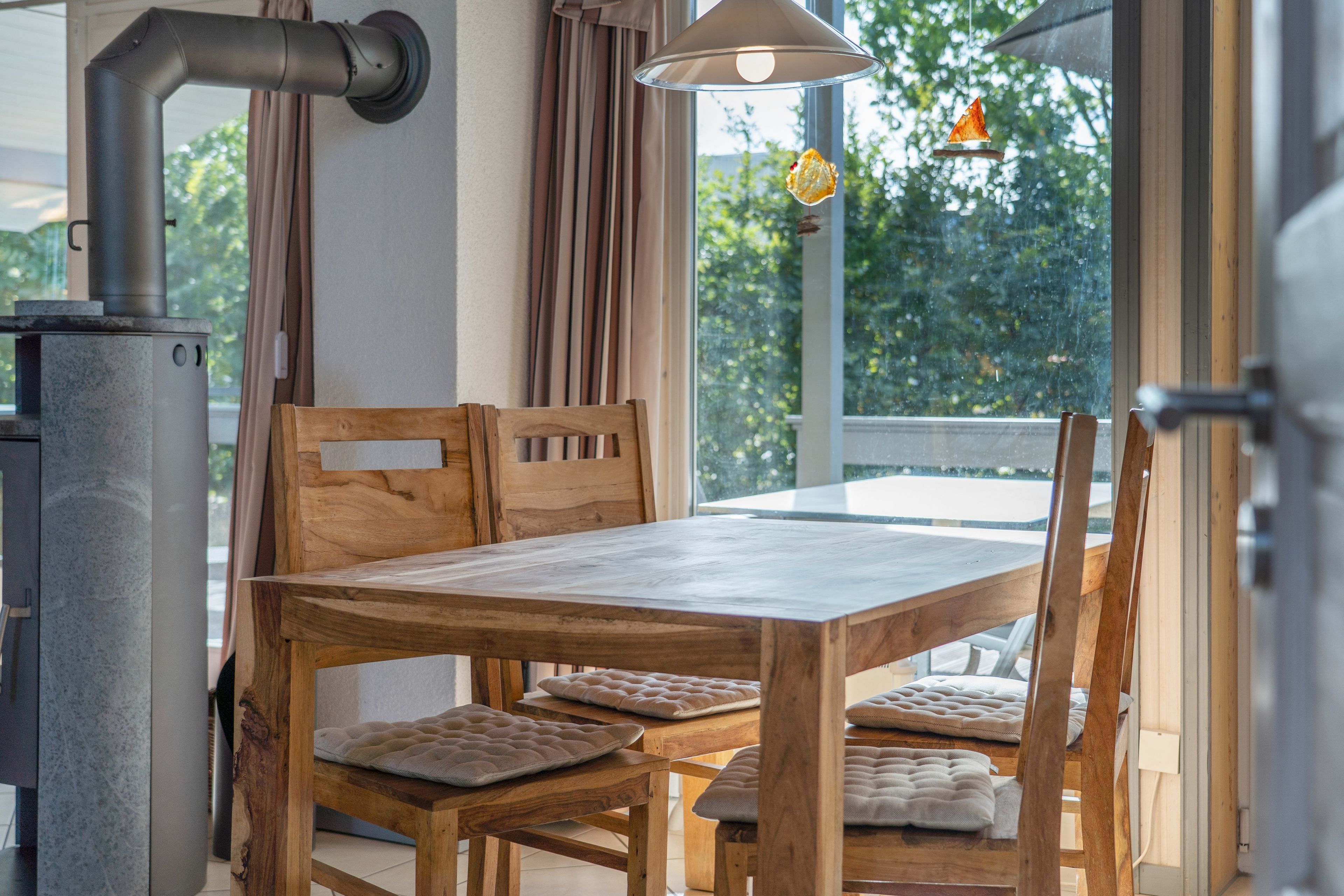 Ein Holztisch mit gepolsterten Stühlen, ein Fenster mit Vorhängen und eine Hängelampe.
