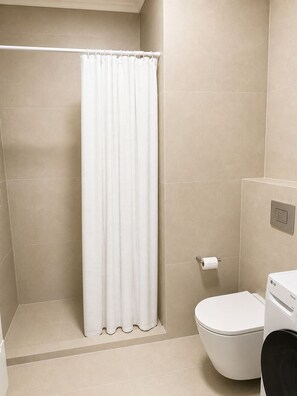 A bathroom with a shower curtain, toilet, and a wall-mounted paper towel dispenser. - Vrbo Property (Chișinău)