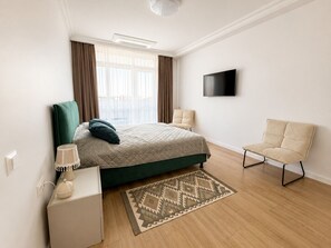 A modern bedroom with a bed, a chair, a TV, and a patterned rug. - Vrbo Property (Chișinău)