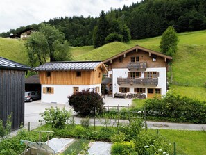 Un chalet à deux étages doté d’un balcon, entouré d’une végétation luxuriante et situé dans un paysage vallonné.