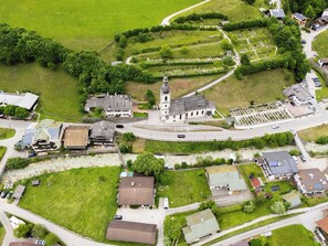 Luchtbeeld van een dorp met een opvallende kerk, kronkelende wegen en woonhuizen.