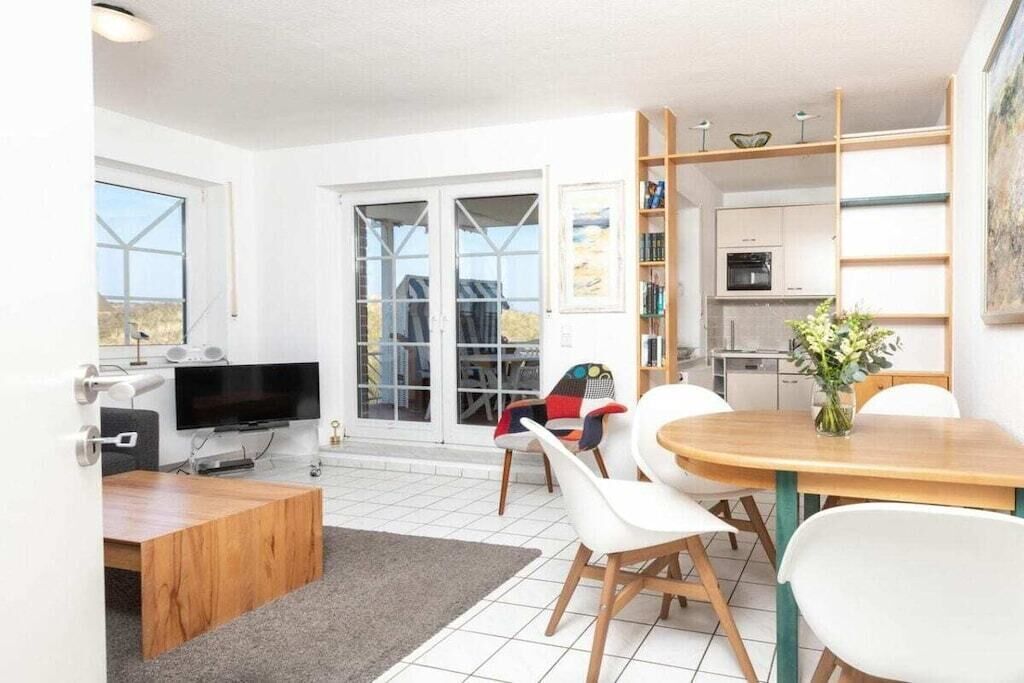 Un salon moderne avec un téléviseur, un coin repas avec une table et des chaises, et une cuisine équipée de placards et d’un four à micro-ondes.