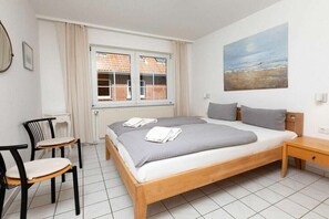A bedroom with a bed, two chairs, a nightstand, a window with curtains, and a painting on the wall. - Holiday apartment in Juist with swimming pool (Juist)