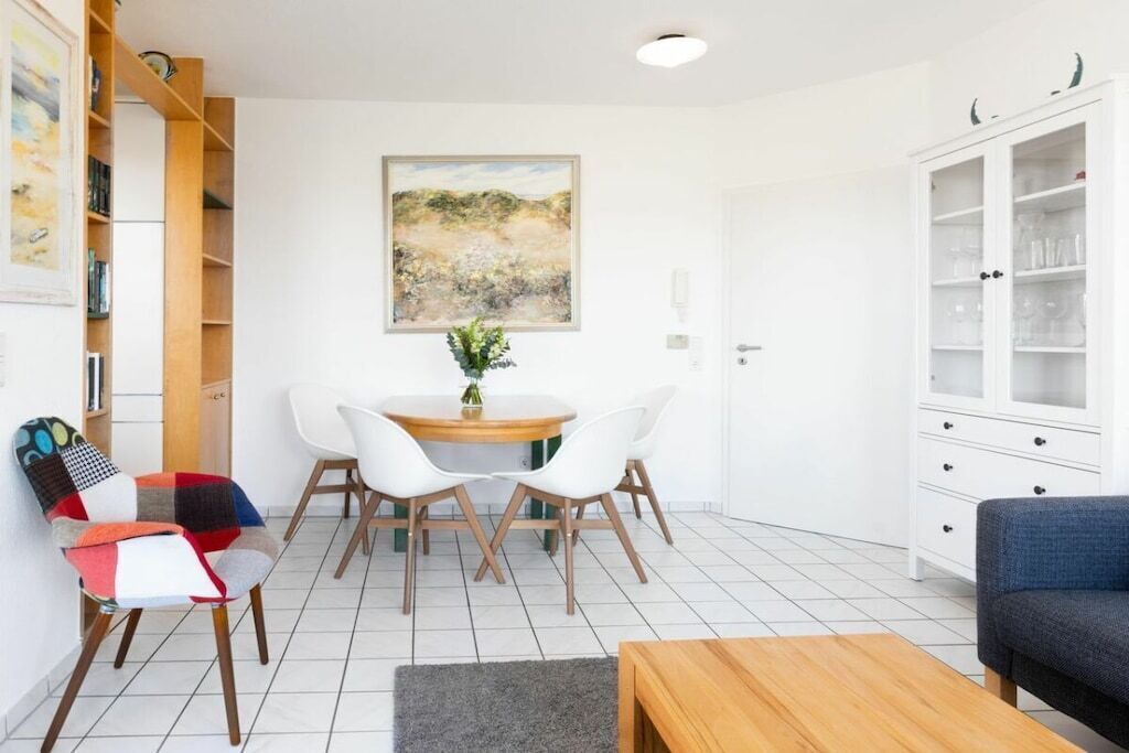 A modern living room with a dining area, white walls, and a large painting.