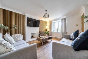 Ein modernes Wohnzimmer mit Flachbildfernseher, einer Chandelüster und einer Sofagarnitur.