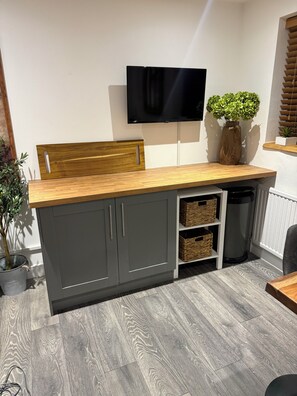 A compact kitchen with a wooden countertop, grey cabinets, and a mounted television. - House Sleeps 4 With Parking and Garden (Scunthorpe)