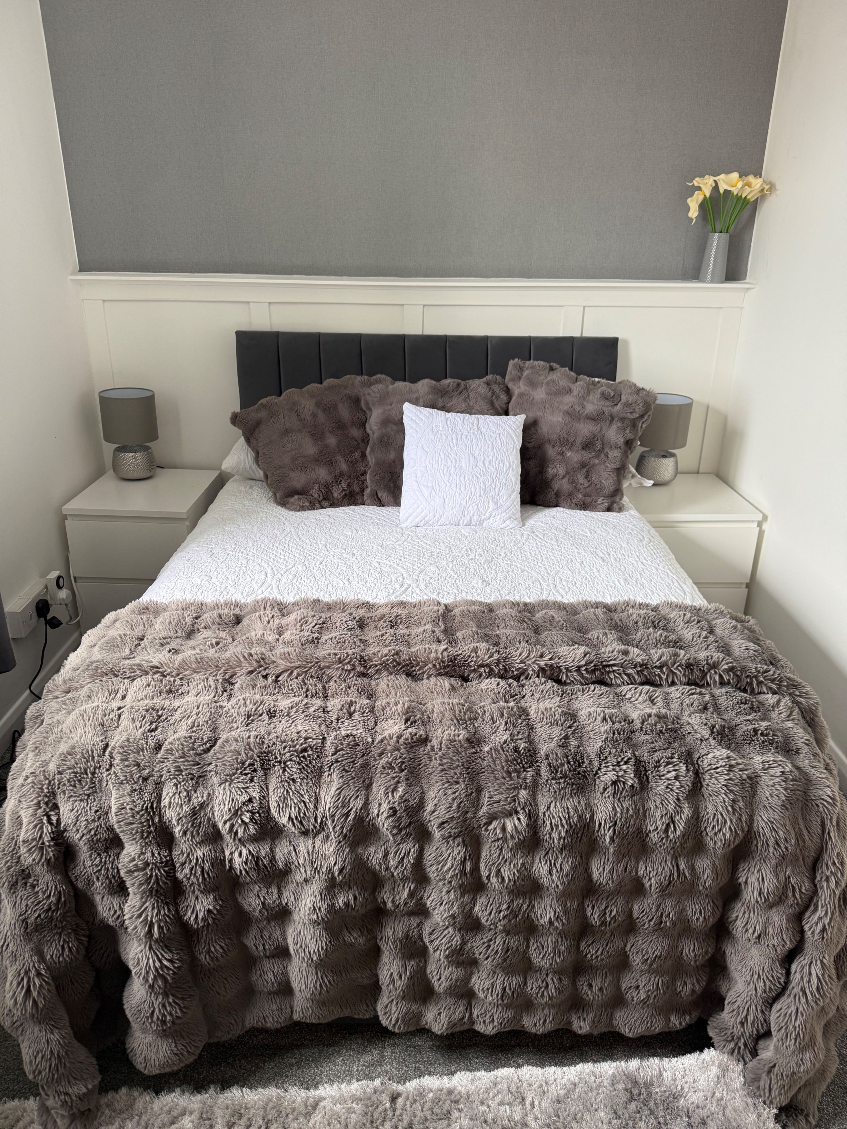 A bed with a white and brown textured duvet, two bedside lamps, and a grey headboard.