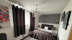 Ein Schlafzimmer mit einem Bett, einer Kristallleuchter, einem grauen Sofa, einem Teppich und einem Gemälde an der Wand.