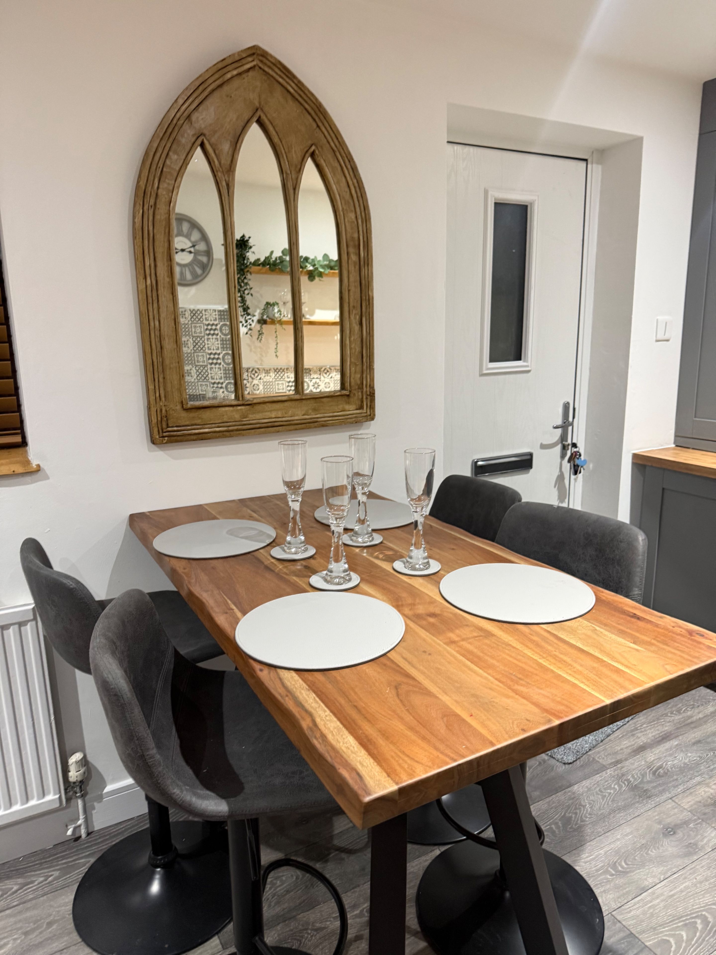 A dining area with a wooden table set for four, surrounded by four chairs.