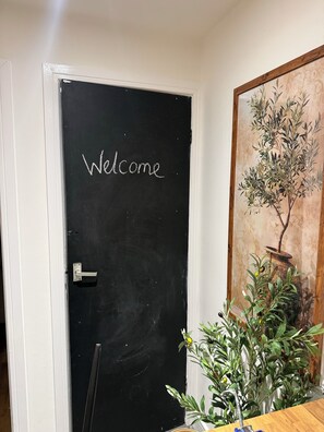 A black door with 'Welcome' written on it, a white door frame, and a potted plant with green leaves and a brown pot. - House Sleeps 4 With Parking and Garden (Scunthorpe)