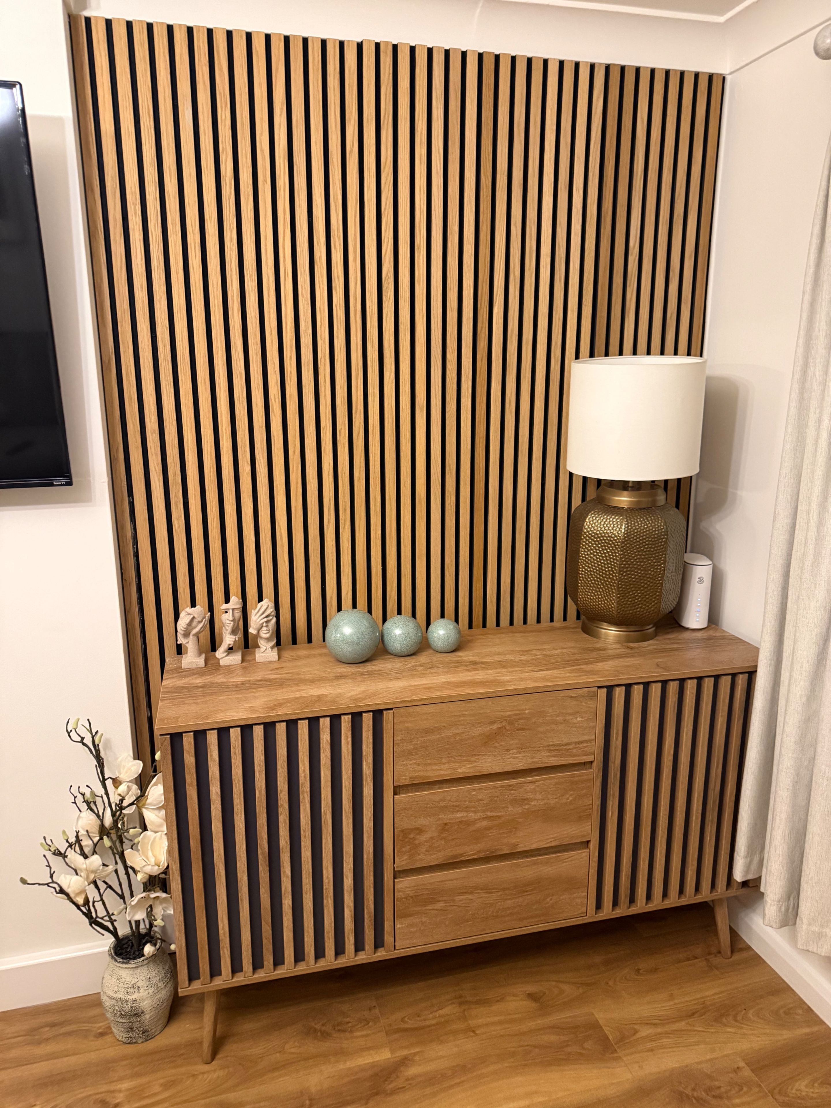 A wooden console table with a slatted back panel, a lamp, and decorative items.
