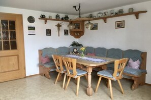 Un coin repas comprenant une table en bois, six chaises, un banc et une étagère murale où sont disposés divers objets.