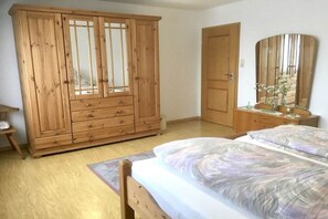Une chambre à coucher avec une armoire en bois, un lit recouvert d’une couvre-lit à motifs, une table de chevet et un miroir.