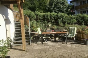 Une terrasse extérieure avec une table et des chaises en bois, entourée de plantes en pot et d’une clôture en bois.