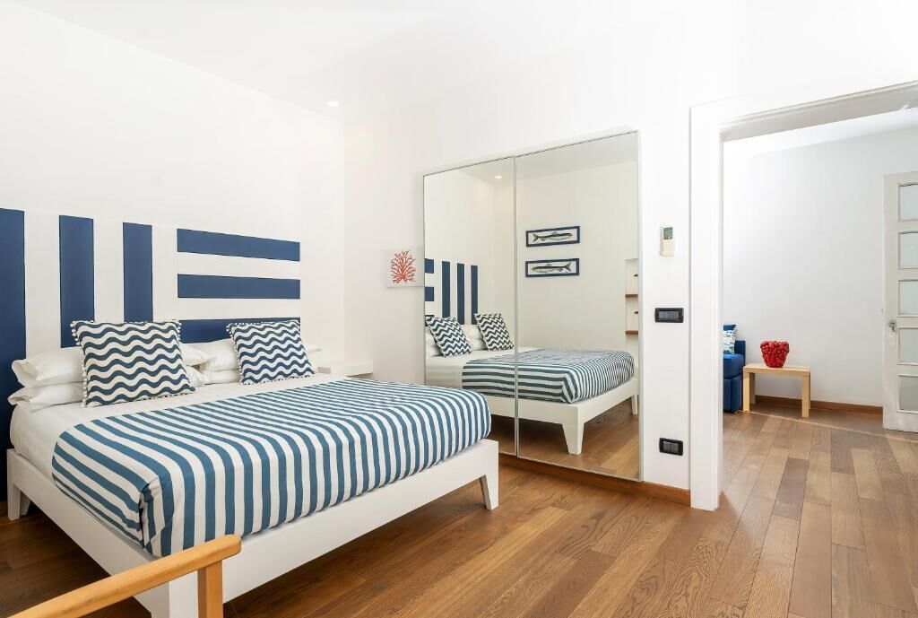 A bedroom with a bed, a mirror, and a wooden floor.