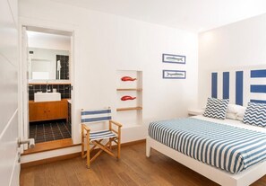 Ein Schlafzimmer mit einem Bett, einem Sessel, einem Regal mit Dekoration und einer Tür zu einem Badezimmer.