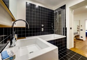 Ein modernes Badezimmer mit einem großen weißen Waschbecken, einer Dusche und schwarzen Fliesenwänden.