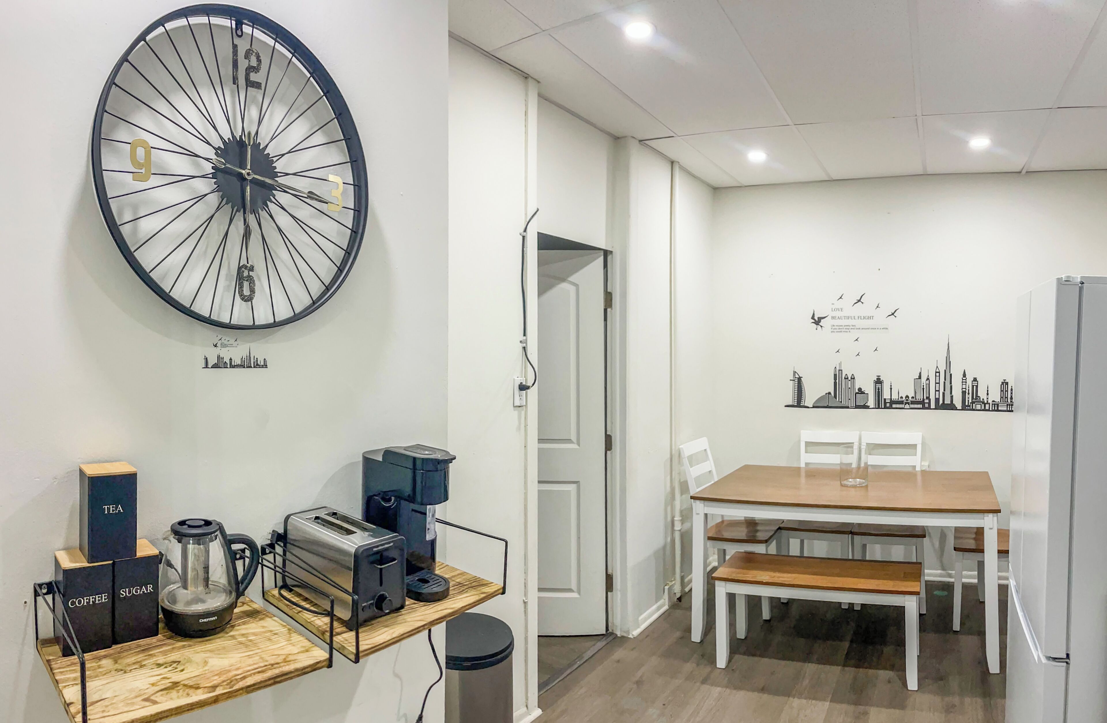 Une cuisine moderne avec une grande horloge, une machine à café, un grille-pain et une bouilloire posés sur un plan de travail en bois.
