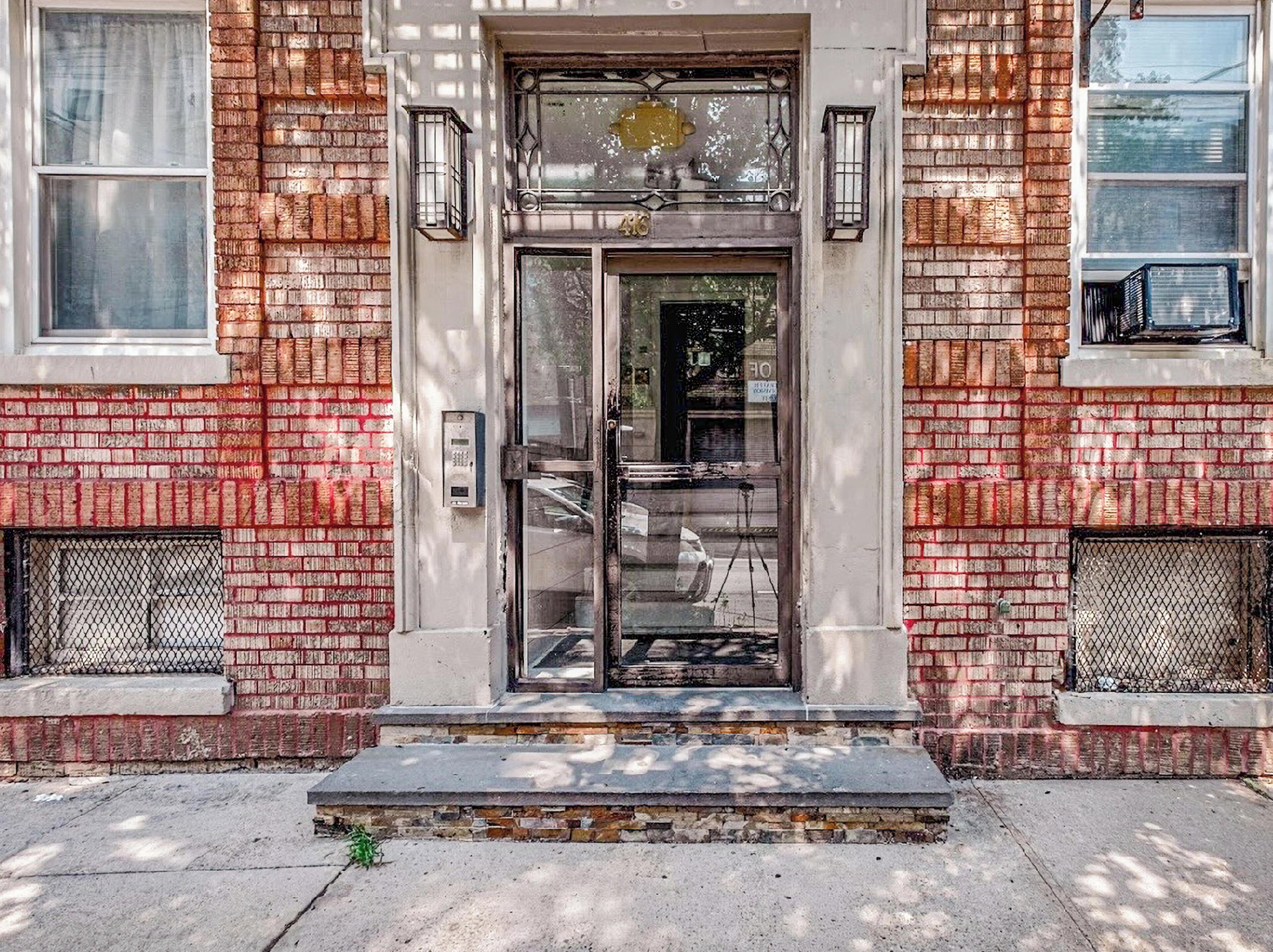 A brick building with a glass door entrance, a metal gate, and a small set of steps leading up to the door.