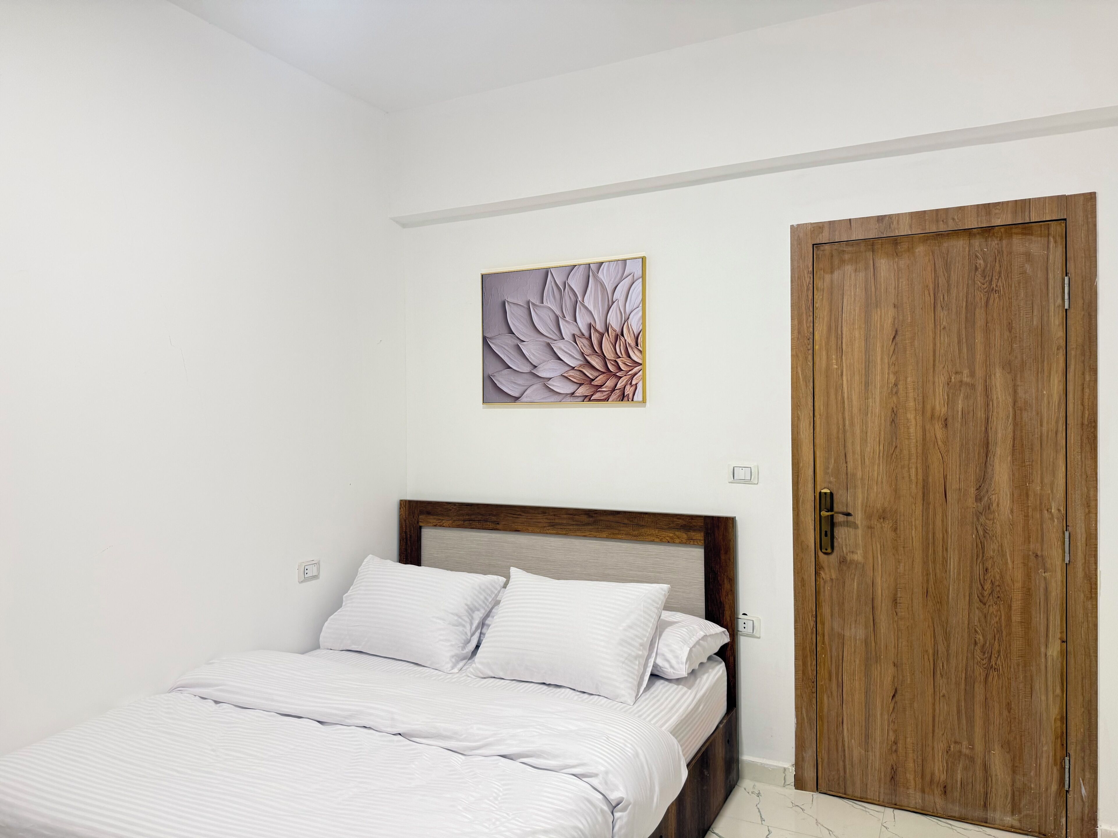 A bedroom with a bed, a wooden door, and a wall-mounted artwork.