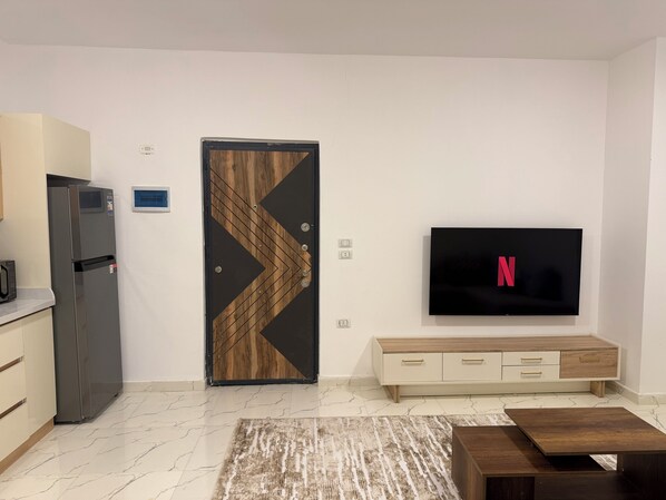 Un salon moderne doté d’un téléviseur à écran plat, d’une porte en bois au motif géométrique, d’un meuble télé intégré et d’un sol en marbre.