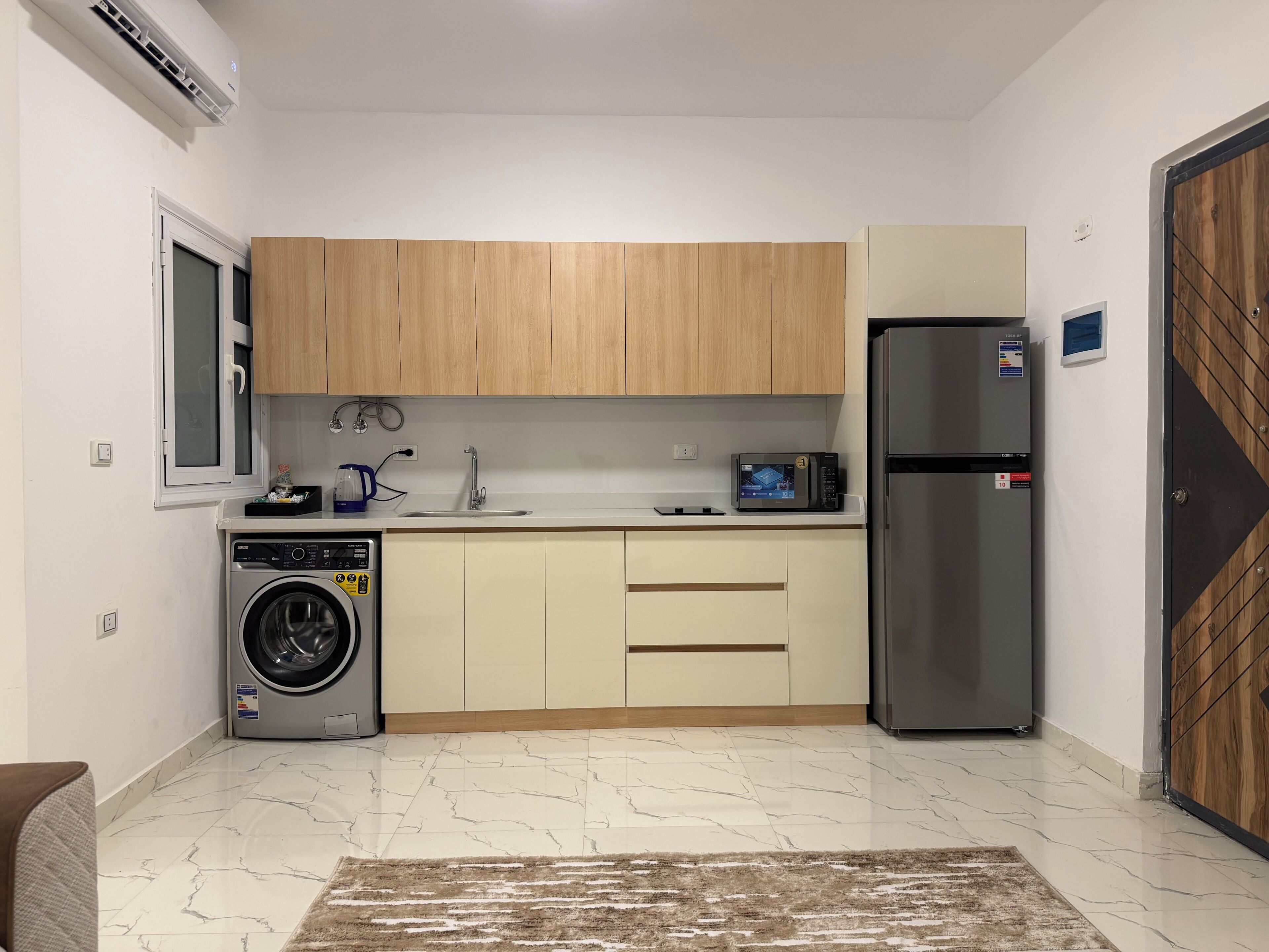 A compact kitchen with a washing machine, a refrigerator, and wooden cabinets.
