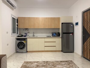 A compact kitchen with a washing machine, a refrigerator, and wooden cabinets. - Charming Apartment in the heart of Hurghada (Hurghada)