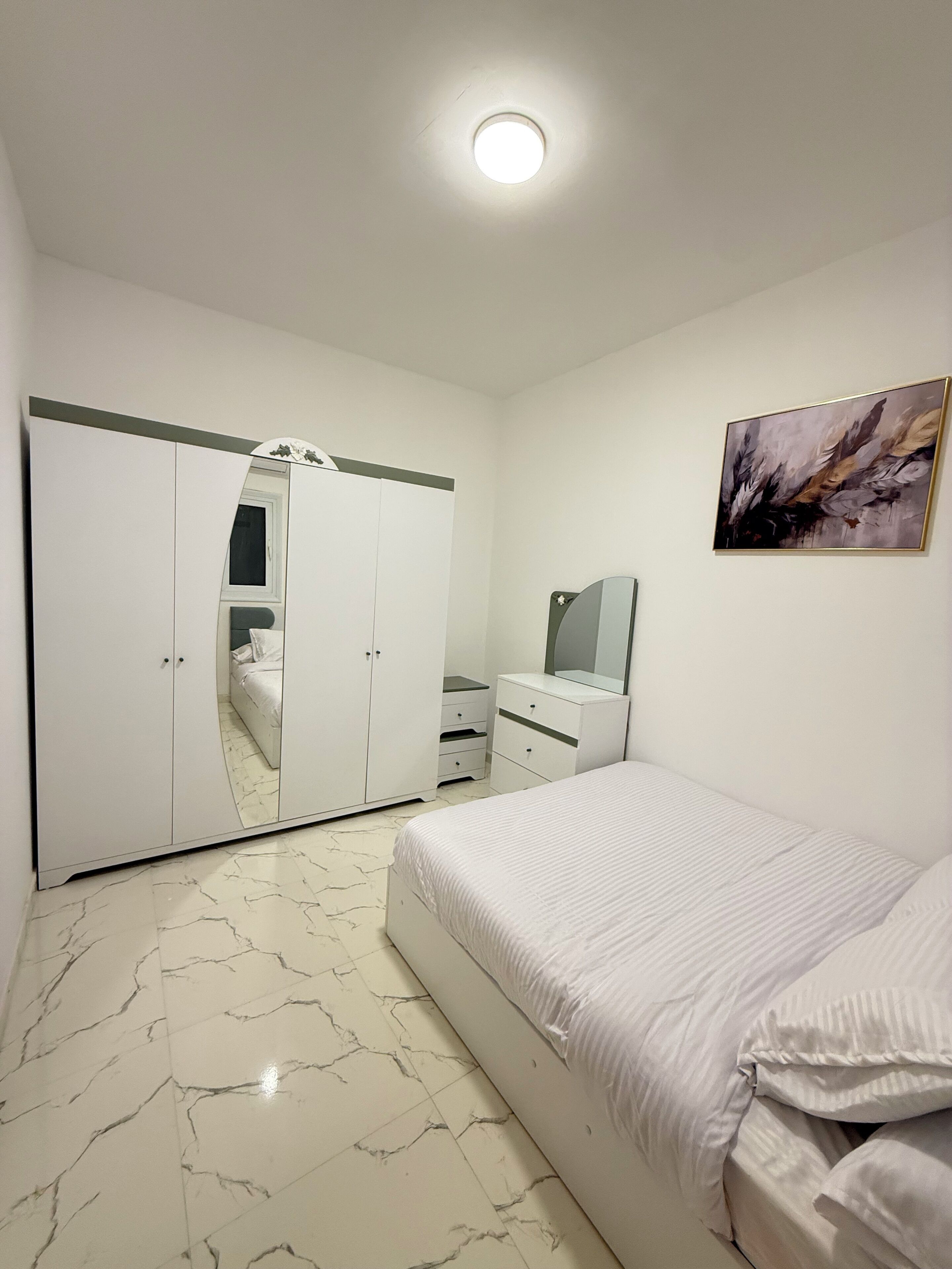 Une chambre à coucher avec un lit, une armoire, une commode, un miroir et un tableau accroché au mur.