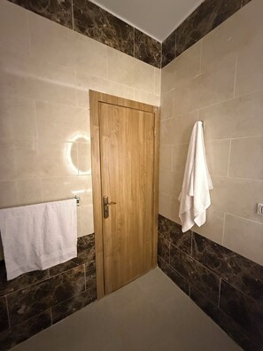 Une salle de bain avec une porte en bois, une serviette blanche posée sur un porte-serviettes et une autre serviette blanche accrochée au mur.