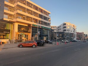 Un immeuble à plusieurs étages doté de balcons, un restaurant appelé « Oriental Food » et un parking où sont stationnées plusieurs voitures.