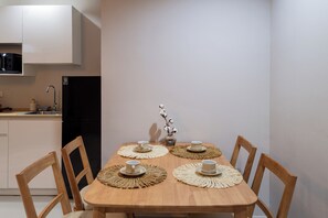 Una mesa de comedor con cuatro sillas, un florero con plantas de algodón y un refrigerador negro al fondo.