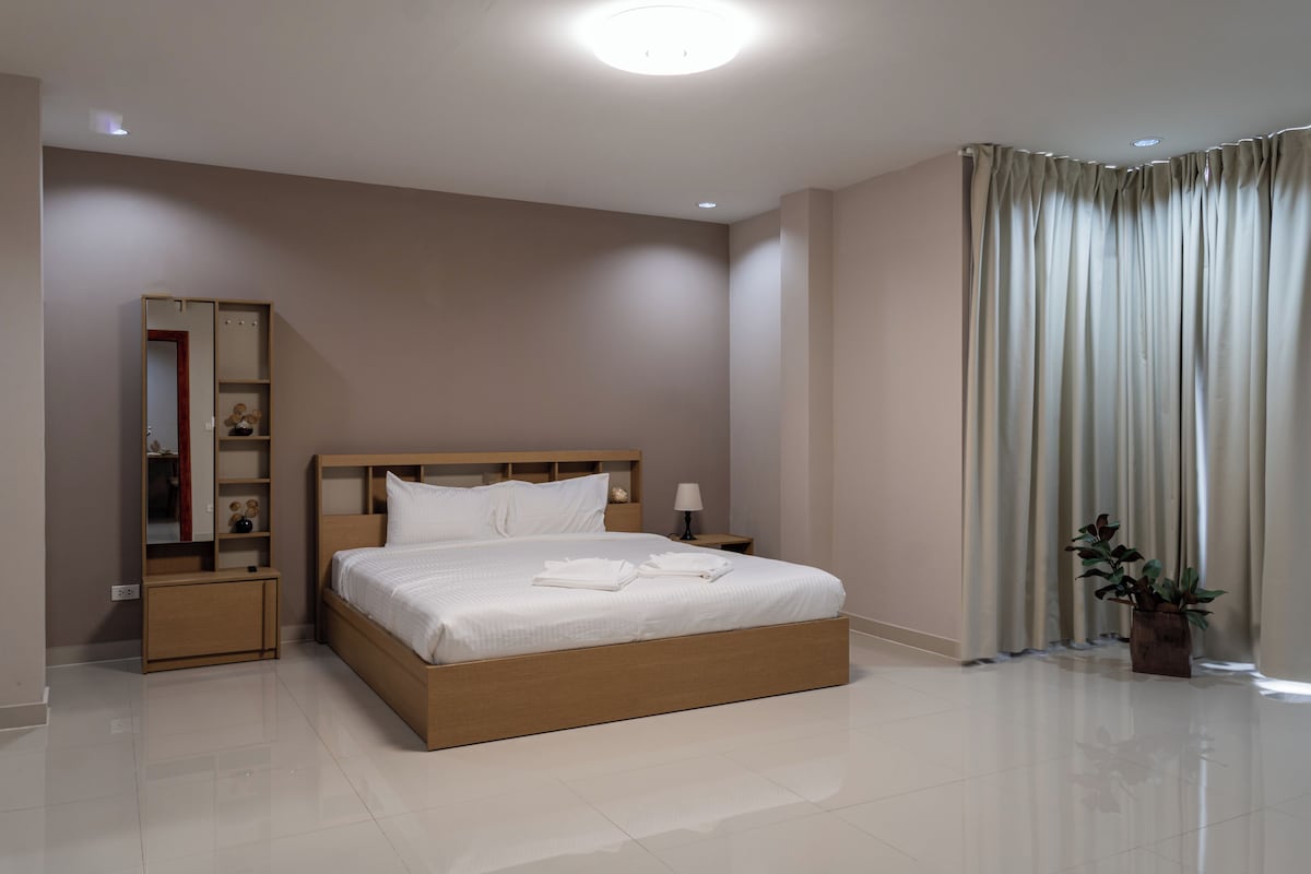 A modern hotel room with a large bed, a bedside table, a nightstand, a mirror, and a potted plant.