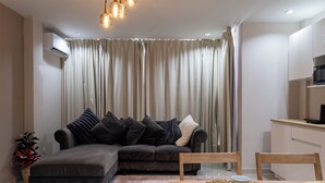A modern living room with a sectional sofa, a dining table with a placemat, and a kitchen area with a microwave. - The one Sky (Phuket)
