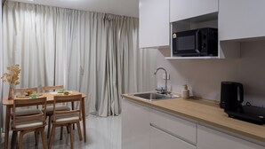 A modern kitchen with a dining table, chairs, a microwave, a coffee maker, and a sink. - The one Sky (Phuket)