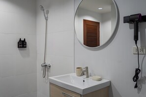 A bathroom with a white sink, a mirror, a shower, and a hairdryer on the wall. - The one Sky (Phuket)