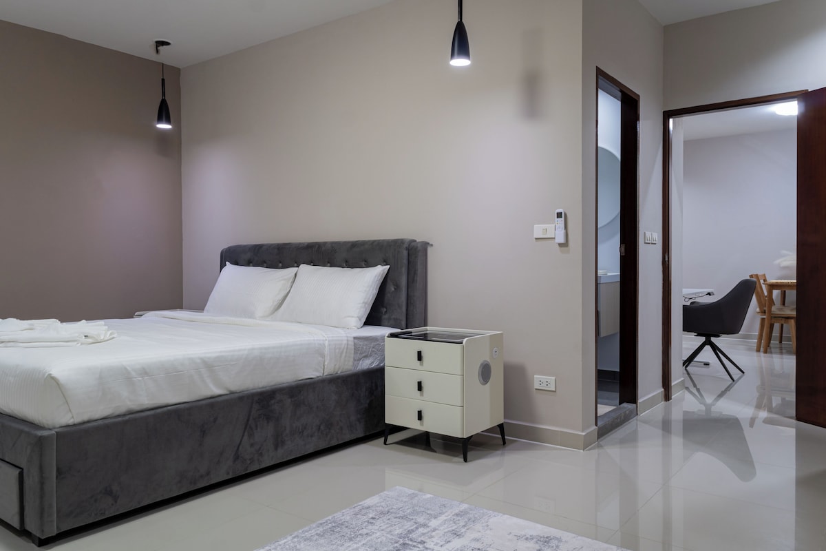 A modern bedroom with a bed, bedside tables, a mirror, and a view of a bathroom.