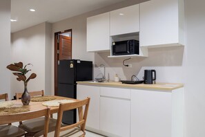 A compact kitchen with a refrigerator, microwave, and a kettle on the counter. - The one Sky (Phuket)