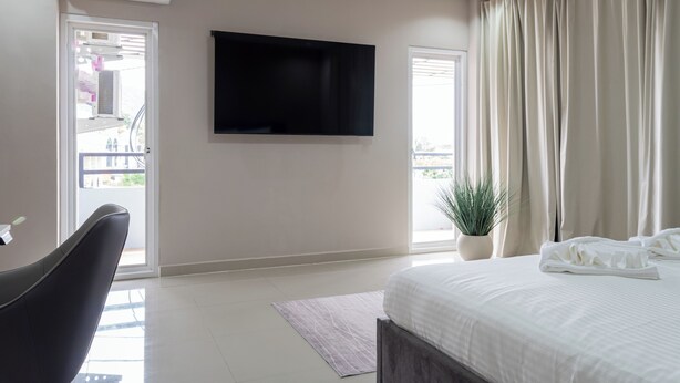 A hotel room with a bed, a flat-screen TV, a potted plant, and a balcony door. - The one Sky (Phuket)